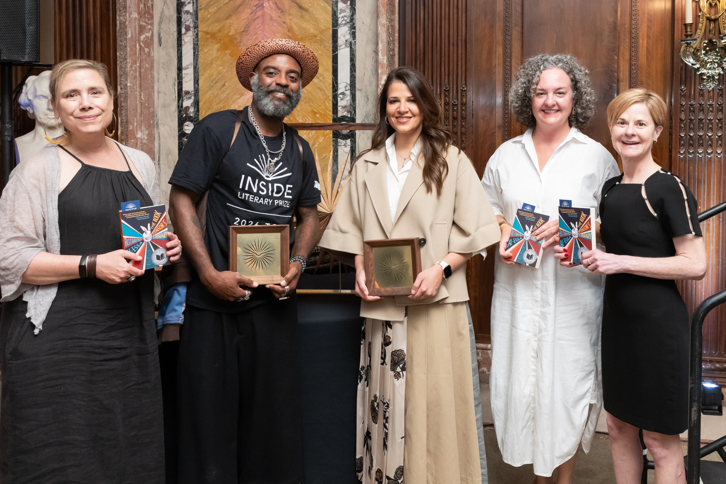 5 people standing. Some are holding books; some are holding an award.