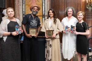 5 people standing. Some are holding books; some are holding an award.